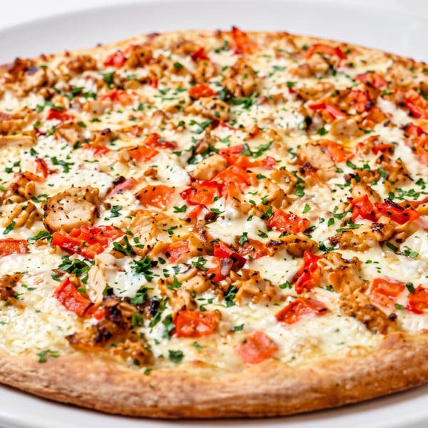 Close-up of a white pizza topped with chicken, red peppers, and parsley on a white plate.